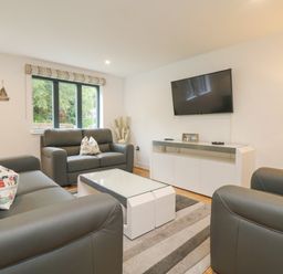 A living room with grey leather sofas a white coffee table a striped rug a wall-mounted television and windows at Bluebell Retreat in Lostwithiel