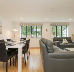 A dining area with a table set for six and a living area with two gray sofas and windows at Bluebell Retreat in Lostwithiel