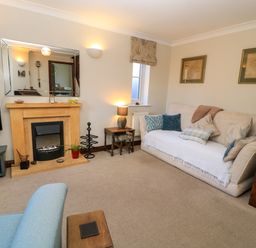 A living room with a sofa next to stairs a fireplace a mirror and a television at Oakmead in Moreton-In-Marsh
