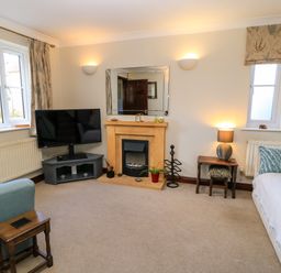 A sitting room with a fireplace tv two windows and sofas at Oakmead in Moreton-In-Marsh