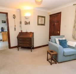 A sitting room with a blue armchair a small wooden side table and a wooden writing desk at Oakmead in Moreton-In-Marsh