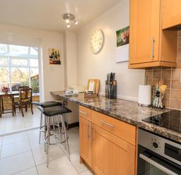 A kitchen with wooden cabinets and countertop bar stools beside a dining area with a wooden table and chairs at Oakmead in Moreton-In-Marsh