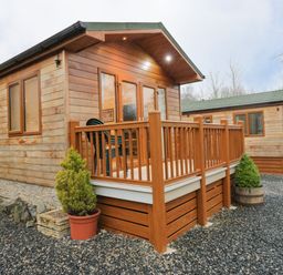 A wooden cabin with a porch and potted plants surrounded by gravel at 8 Woodlands in Water Yeat Coniston Water