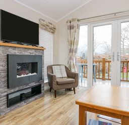 A living room with a fireplace a TV armchair wooden table and glass doors leading outside at 8 Woodlands Water Yeat Coniston Water
