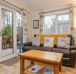 A living room with a brown leather sofa and a wooden coffee table next to glass doors at 8 Woodlands Water Yeat Coniston Water