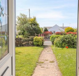 View from an open door showing a garden path leading to a road with shrubs and a white house in the background at Bryntirion in Moelfre