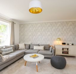 A living room with a gray sectional sofa a white round coffee table a gray pouf a sideboard with a lamp and small plants at Bryntirion in Moelfre