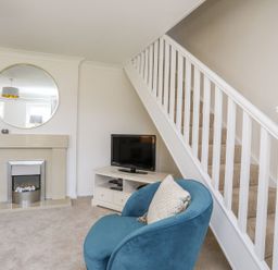 A living room with a blue chair a fireplace and TV under stairs at Bryntirion in Moelfre