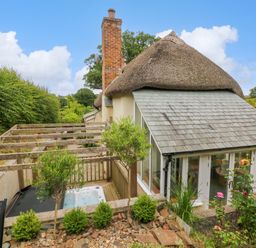 An outdoor area with a wooden pergola and hot tub next to a thatched cottage with a slate roof at Rose Cottage in Okehampton