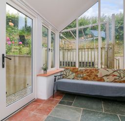 A room with glass doors a sofa and tiled floor at Rose Cottage in Okehampton