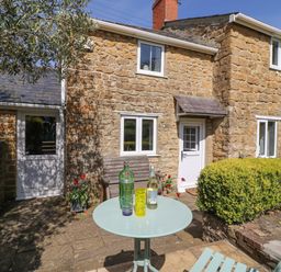 A stone cottage exterior with a small patio table and chairs and a wooden bench at Tiddlers Cottage in Uploders near Bridport