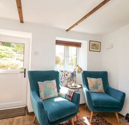A sitting area with two blue armchairs next to a small window and door at Tiddlers Cottage in Uploders near Bridport