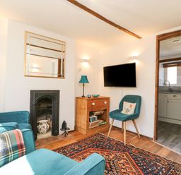 A sitting room with teal armchairs a wooden cabinet a fireplace and a wall mounted television at Tiddlers Cottage in Uploders near Bridport