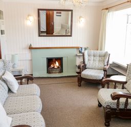 A sitting room with a fireplace three armchairs a sofa and a window at Sea Watch House in Roundstone County Galway