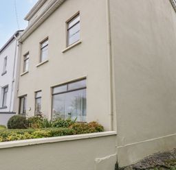Exterior view of a two-story cream colored house with windows and garden at Sea Watch House in Roundstone County Galway
