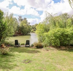 A garden with two black chairs facing a lake surrounded by trees at Lakeside Lodge Retreat in Tattershall