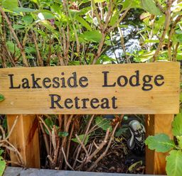 A wooden sign with Lakeside Lodge Retreat surrounded by green plants and shrubs in a garden