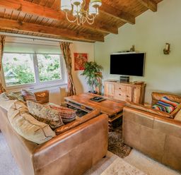 A living room with leather sofas wooden coffee table mounted TV and a window with curtains at Lakeside Lodge Retreat in Tattershall