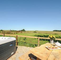 An outdoor area with a hot tub a wooden table with a teapot cups and scones overlooking a grassy field at Orchard Retreat in East Worlington near Witheridge