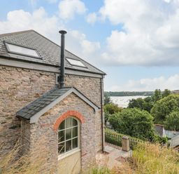 A stone building with two skylights and chimney near a river and trees at The Old Chapel in Dittisham