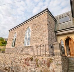 Exterior view of a stone building with arched windows and wooden door with steps at The Old Chapel in Dittisham