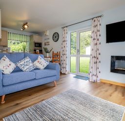 A living room with a blue sofa next to glass doors and a wall-mounted television at Woodside in Rosecraddoc near St Cleer