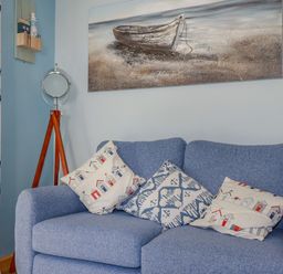A blue sofa with three decorative pillows a standing mirror a painting of a boat on the wall and curtains with sailboat patterns at Woodside in Rosecraddoc near St Cleer