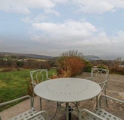 A patio with a round metal table and four chairs overlooking a grassy field and hills at Ceunant near Newport