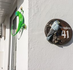 A white wall with a door and a green lizard decoration next to a circular plaque with a bird and the number 41 at Smugglers in Liskeard near St Cleer