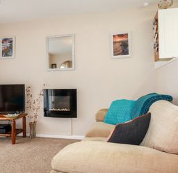 A living room with a beige sofa a television on a wooden stand and framed pictures on the wall at Smugglers Liskeard near St Cleer