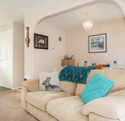 A beige sofa with blue and rabbit cushions in a living room open to a dining area with a table and chairs at Smugglers Liskeard near St Cleer
