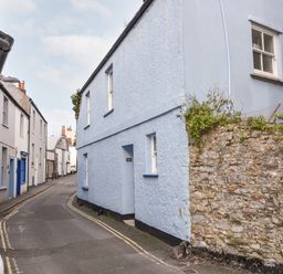 A narrow street with pastel colored houses and a stone wall at Naunton Cottage in Lyme Regis