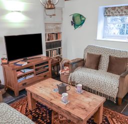 A living room with a wooden coffee table mugs teapot sofas a television on a wooden stand and a window at Naunton Cottage in Lyme Regis