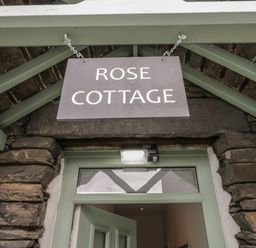 A hanging sign reading Rose Cottage above a green door in a stone wall