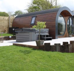 A garden with a wooden curved cabin a hot tub potted plants and wooden fencing at Creuddyn in Llanfihangel-y-Creuddyn near Aberystwyth