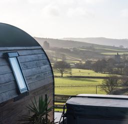 A wooden cabin with a window and a covered hot tub overlooking green fields and hills at Creuddyn in Llanfihangel-y-Creuddyn near Aberystwyth