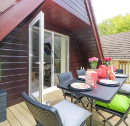 An outdoor dining area with a black table and chairs on a wooden deck at 17 Valley Lodges in Gunnislake
