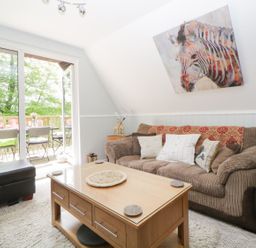 A living room with a brown sofa white pillows wooden coffee table and glass door opening to a balcony at 17 Valley Lodges in Gunnislake