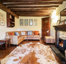 A living room with a leather corner sofa a wooden fireplace a cowhide rug and wooden beams on the ceiling at Gwengraig Brithdir near Dolgellau