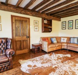 A living room with a brown leather lounge chair a curved leather sofa with cushions a wooden door framed pictures on the walls a small wooden table wooden floor and exposed wooden ceiling beams at Gwengraig in Brithdir near Dolgellau