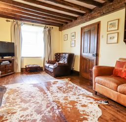 A living room with wooden ceiling beams a leather sofa and armchair a cowhide rug and a television on a wooden cabinet at Gwengraig in Brithdir near Dolgellau