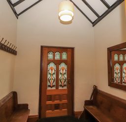 An entryway with wooden benches on either side a wooden door with stained glass panels and a mirror on the wall at Old School Muncaster House in Ravenglass near Holmrook