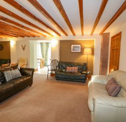 A living room with three sofas two striped cushions a wooden chair a floor lamp exposed wooden ceiling beams and a wall clock at Old School Muncaster House Ravenglass near Holmrook