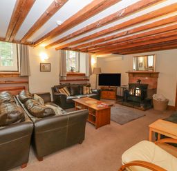A living room with brown leather sofas a wooden coffee table a fireplace and a television at Old School Muncaster House Ravenglass near Holmrook