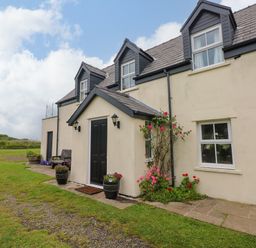 A house with a black door and flowers in planters at North Studdock Cottage, Angle near Pembroke