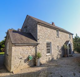 A stone house with a pitched roof and gravel driveway surrounded by plants at Lower Gadles in Burnthouse near Falmouth