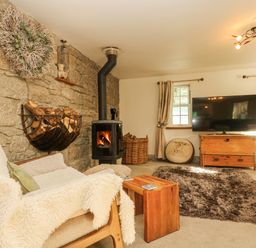 A living room with a wood burning stove and firewood on a stone wall at Lower Gadles Burnthouse near Falmouth