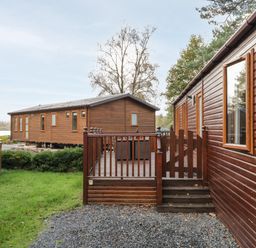 Two wooden lodges with fenced decks and grassy area in between at Wansfell Lodge Pony Meadow 36 White Cross Bay near Windermere