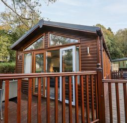 A wooden cabin with a deck and outdoor chairs at Wansfell Lodge Pony Meadow 36 White Cross Bay near Windermere