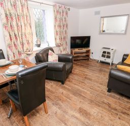 A living room with a dining table set for two armchairs a TV on a wooden stand and a sofa with cushions at The Coach House in St Florence